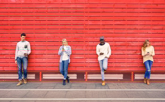 Four people checking their phones against a wall.