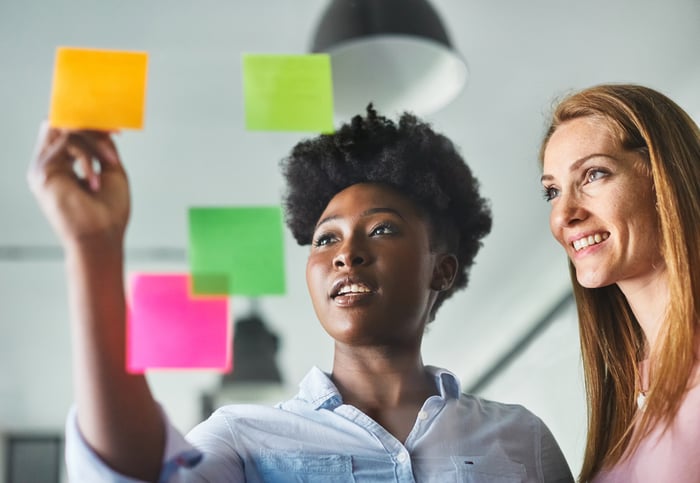 Two people smile while writing on sticky notes. 