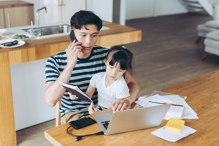 A person talking on the phone and typing on a computer while a child sits on their lap.