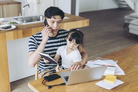 A person talking on the phone and typing on computer while a child sits on their lap.