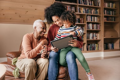 two adults and a child looking at a tablet and smiling