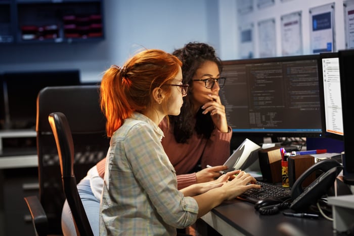 Two computer programmers working together while looking at computer screens.