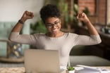 A woman raising her arms in triumph in front of a computer