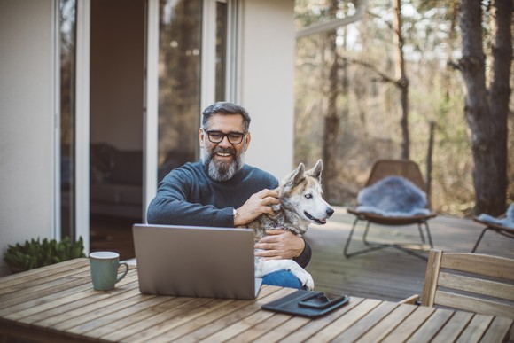 A smiling person at a laptop holding a dog.