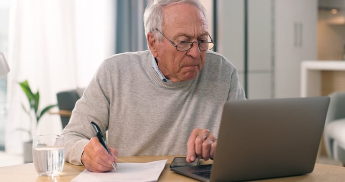 Serious person looking at laptop and taking notes.