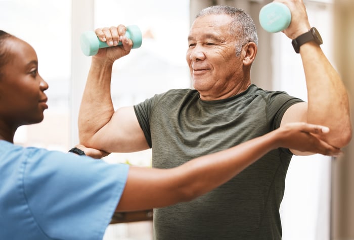 A healthcare worker assisting a patient with hand weights during rehabilitation.
