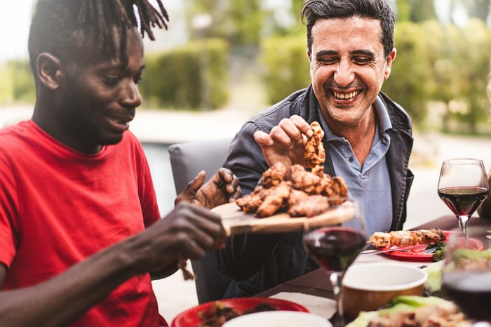 Two people eating chicken wings outside.