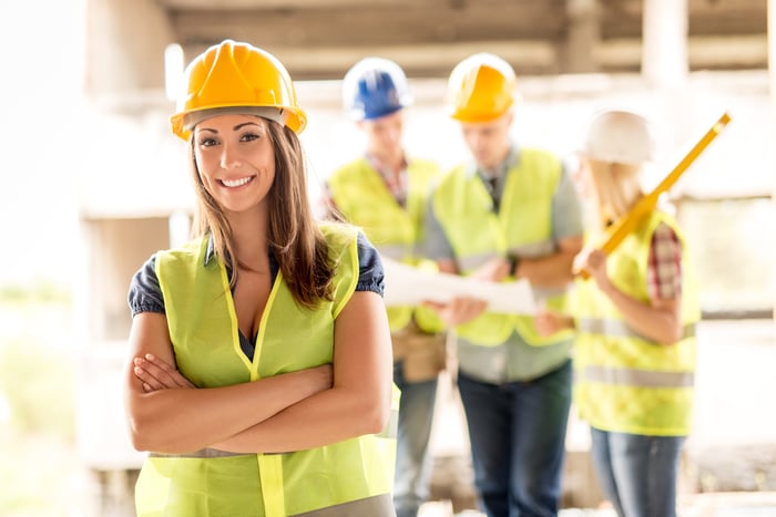 Someone in a hard hat has her arms folded and is smiling at the camera.