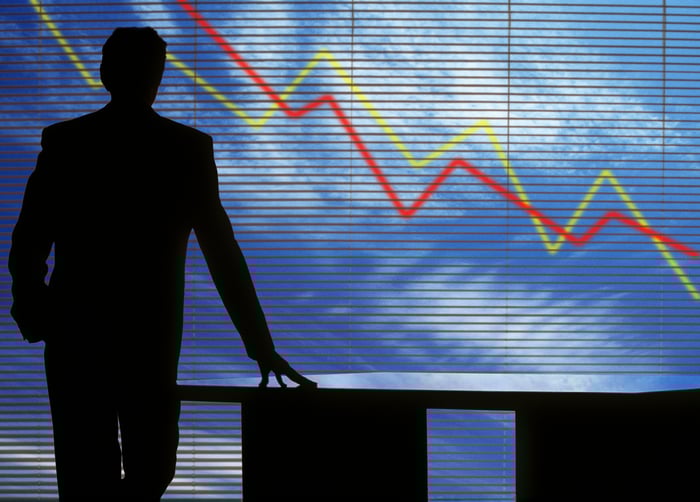 Silhouette of someone standing by a desk and watching stock charts go down.