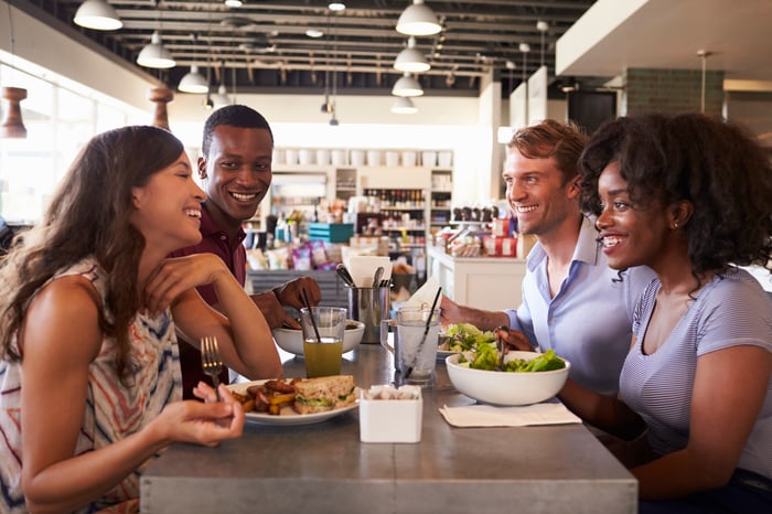 Four friends sitting in a restaurant as a group eating food.