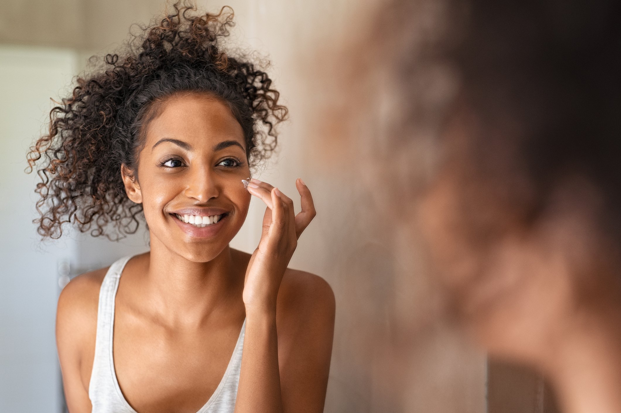 young woman standing in front of mirror applying face cream