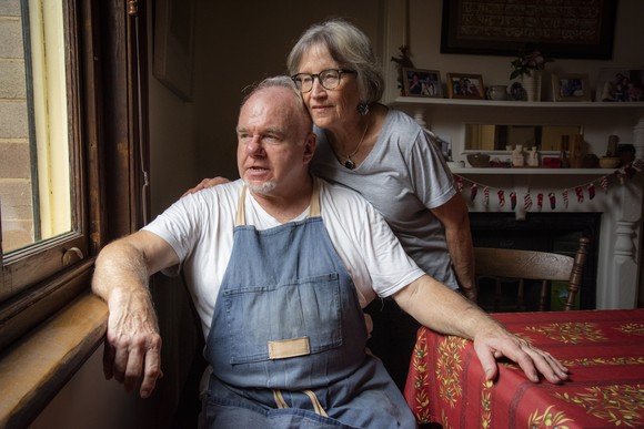 An older couple looking out of their dining room window.