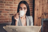 Person drinking coffee and surprised looking at newspaper