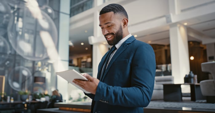 A person wearing professional attire and smiling while holding a tablet in a commercial building.