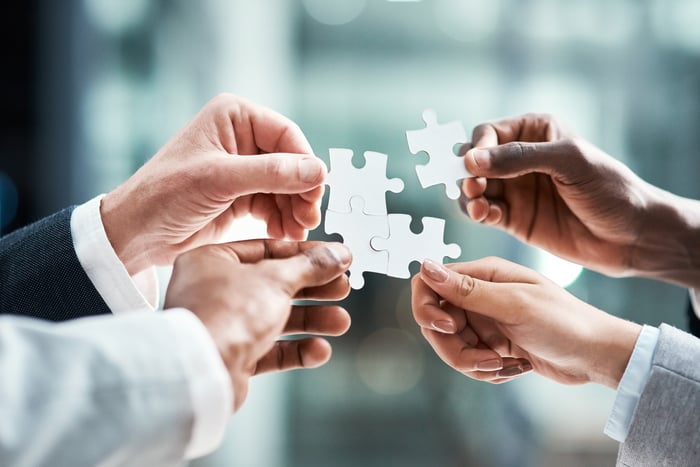 Four hands holding puzzle pieces together.