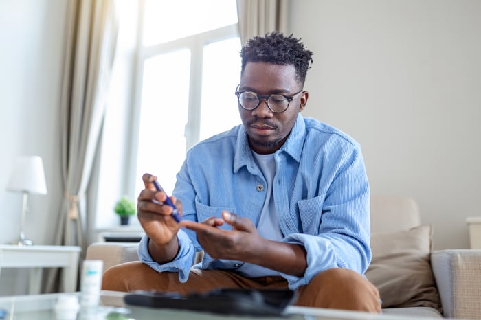 A person sitting on a couch and looking down while holding a pen.