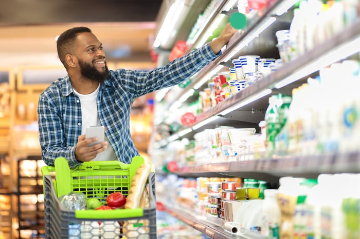 A person smiles while taking a product off a shelf in a grocery store.