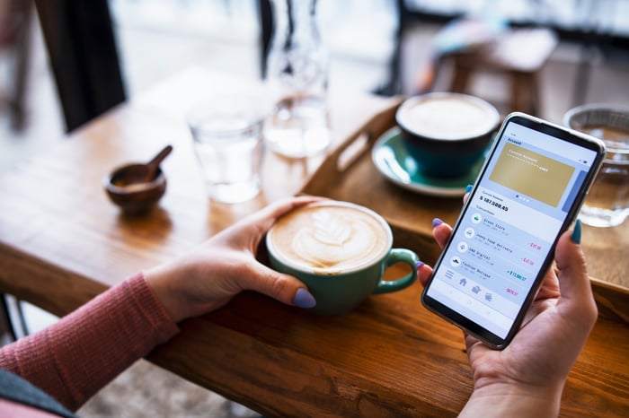 A person looks at a bank app on their phone while drinking coffee in a coffee shop.