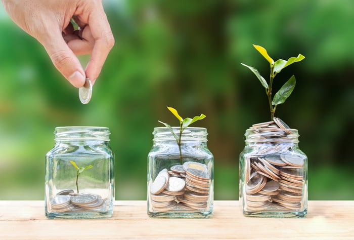 A person putting coins into glass jars that sprout plants based on the number of coins in the jar.
