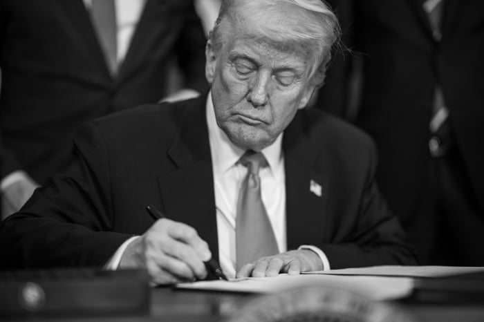 Donald Trump signing an executive order while seated at a desk in the Oval Office.