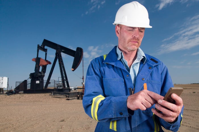 A person wearing protective gear near energy infrastructure using a mobile device.