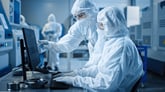 Technicians in lab wearing protective gear looking at computer-1200x675-c2b5ff2