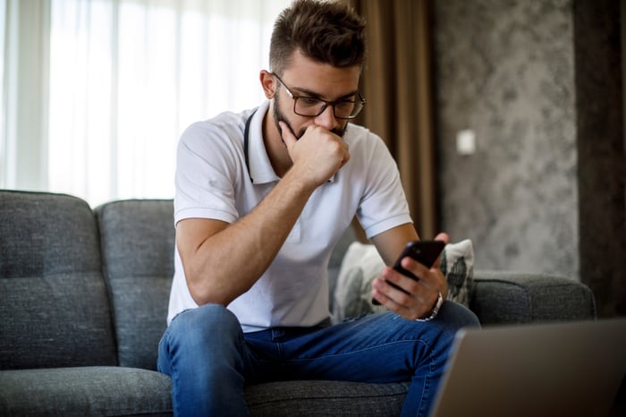 A person sitting on a couch looking at their phone with their first covering their mouth.