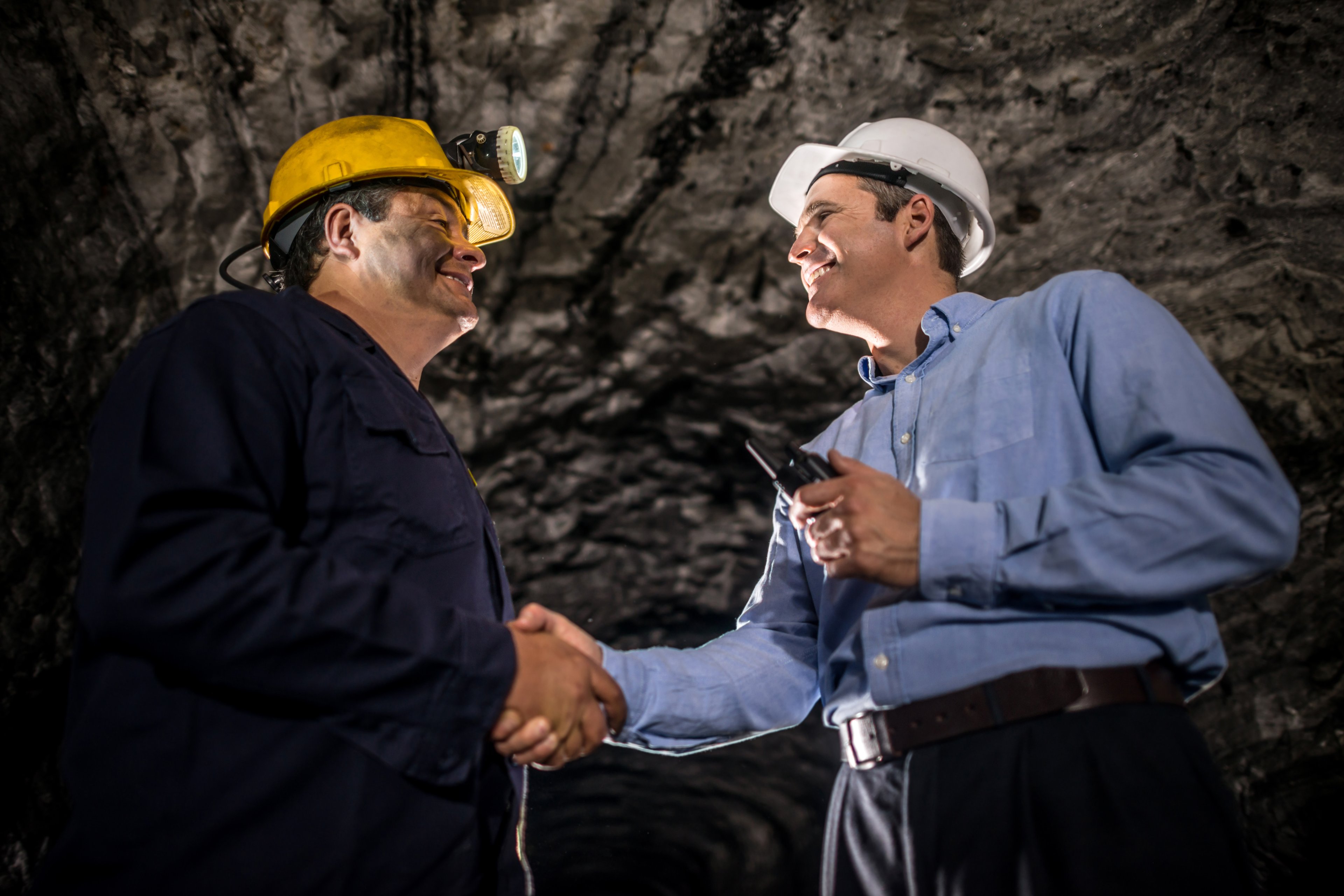 Two people smiling and shaking hands while inside a mine