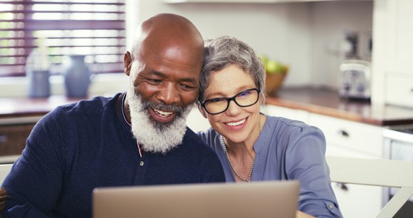 Older couple smiling as they look at a laptop.