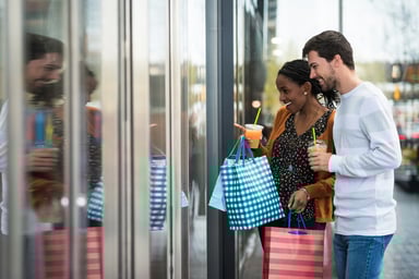 Two people wondow shopping and holding shopping bags in a strip outdoor mall