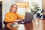 person smiling while sitting at a table and typing on a laptop computer