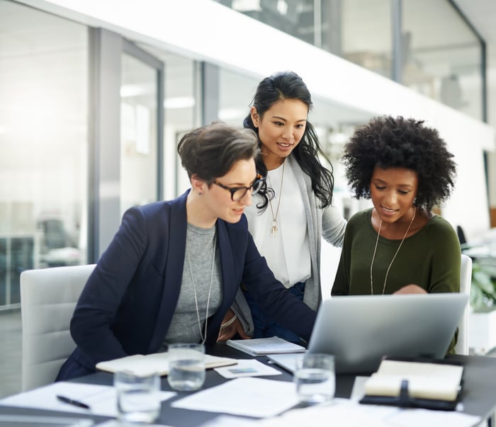 Three investors study something on a laptop in an office.