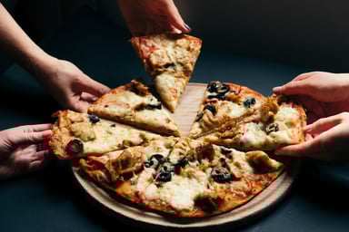 Several hands grabbing slices of pizza from a tray