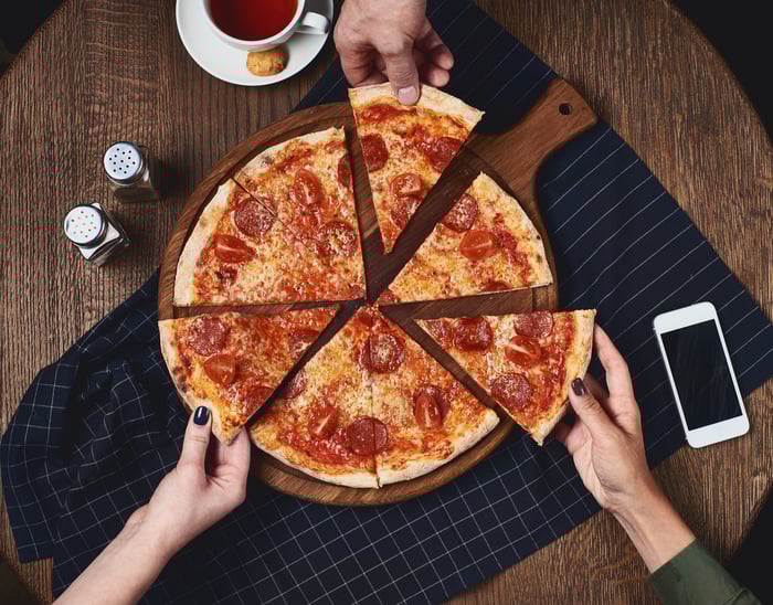 Three people grabbing slices of pizza from a whole pie.