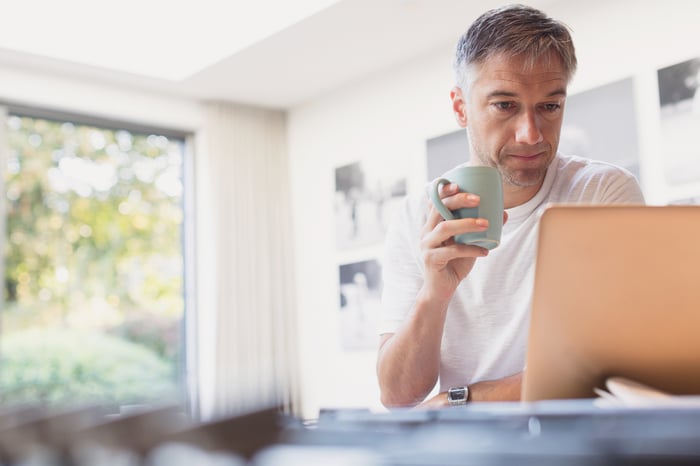 Serious-looking person holding mug and looking at laptop.