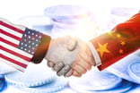 A handshake featuring one arm dressed with an American flag and another with a Chinese flag with coins in the background.