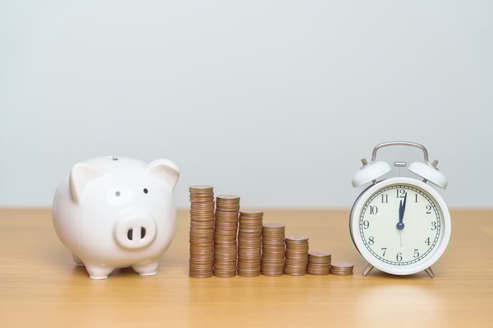 Piggy bank next to a row of stacked coins and a clock. 