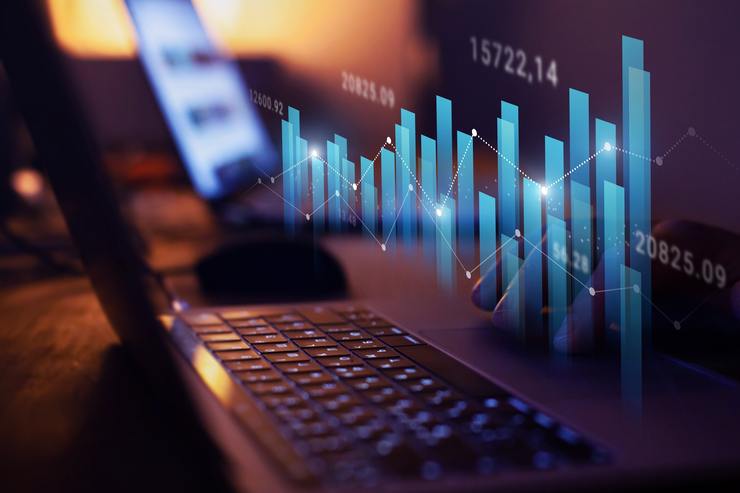 A holographic display of stock charts above a laptop