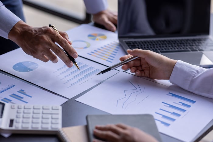 Business people reviewing several papers with charts on a desk with a laptop in the background.