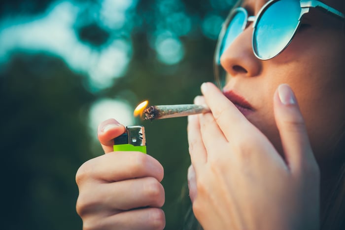 Person wearing sunglasses and lighting a marijuana cigarette.