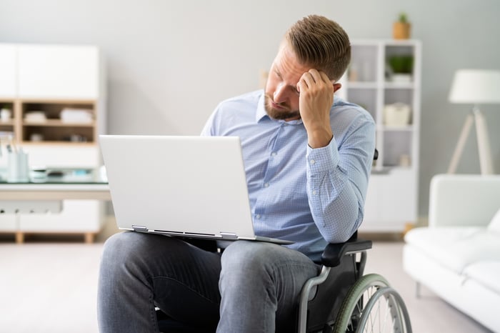 Person in wheelchair looking unhappy while wielding a laptop.