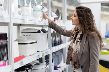 A person smiles while shopping for cooking equipment in a store.