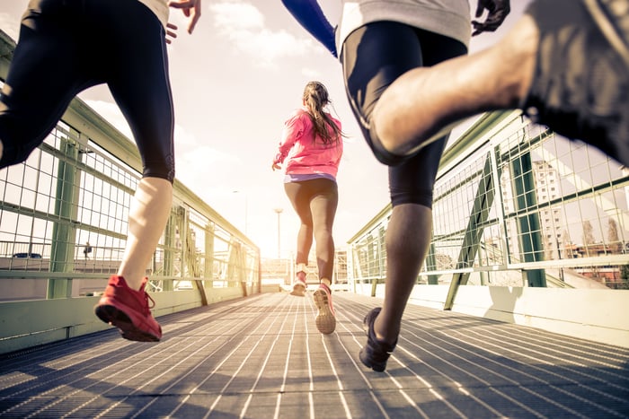Three young people running outdoors on a bridge.