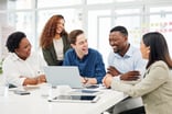 group of people huddled around a computer smiling