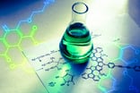 A beaker holding a liquid sitting on top of a sheet of paper with various chemical formulas.