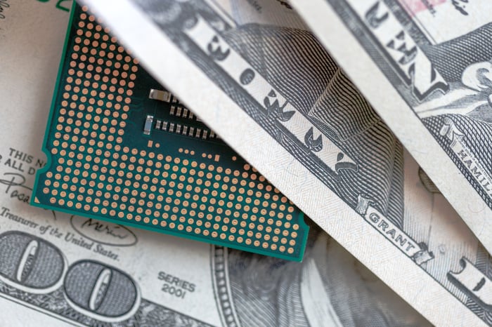 A microchip peeks out from a stack of hundred-dollar bills.