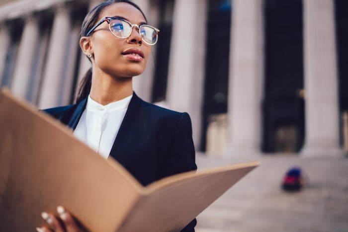 A person in business dress holds an open folder while standing in front of a building with marble columns.