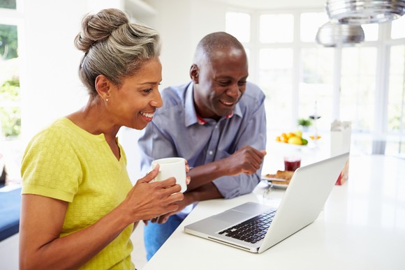 Two people smile while looking at a laptop computer on a counter.