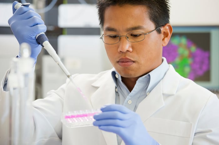A pharmaceutical lab technician using a pipette to fill a test tube tray with liquid samples.
