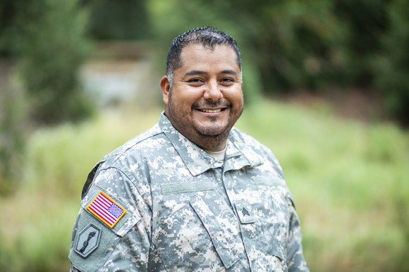 Smiling person in military uniform outdoors.